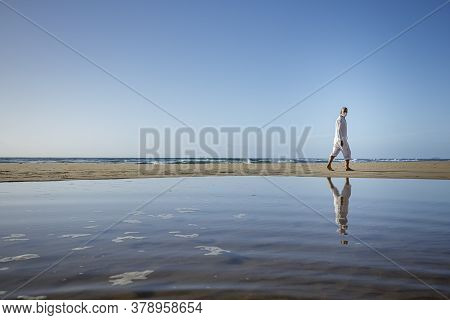Man With Medical Mask Sitting On Beach During Coronavirus Covid 19 Pandemic, Social Distance Concept