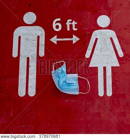 A Crumpled Protective Mask Lies On A Red Sign That Informs People To Keep 6 Feet A Social Distance. 