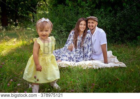 Cheerful Familty At The Park. Cute Little Baby Girl Laughing On Camera And Parents Looking At Her