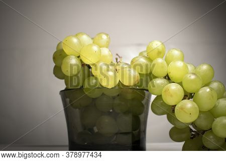 In The Center Of The Photo Green Grapes Lie In A Black Transparent Cup