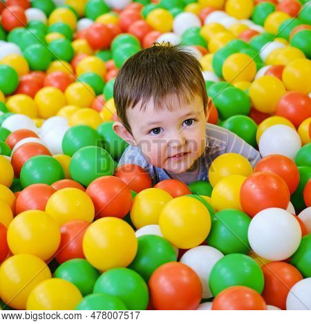 Toddler Baby Plays In The Pool With Balls. Child Boy Crawling In The Pool With Plastic Balls. Kid Ag