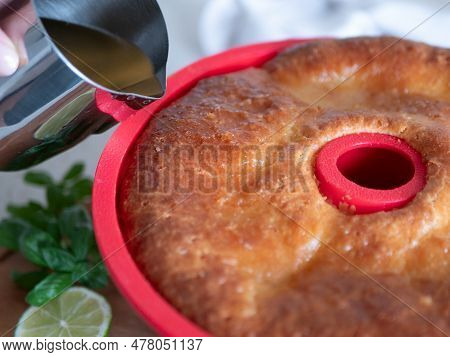 Pouring The Syrup Over The Freshly-baked Rum Baba In Silicone Cake Mold. Rum-soaked Circular Cake Sa