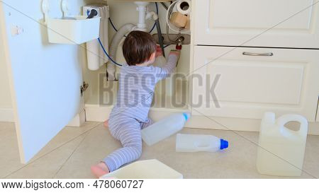 A Child Is Playing With Chemical Cleaning Products Under The Sink In The Kitchen. Baby Holds Bottles