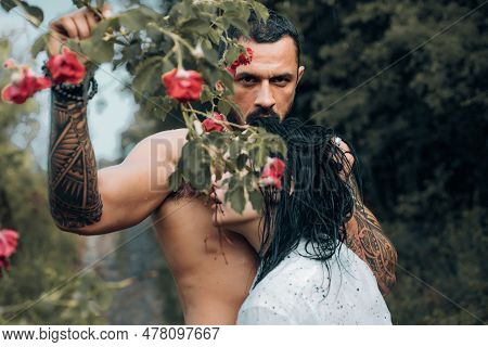 Sensual Cople In Love. Brutal Bearded Man Holding Rose Ramification And Embracing His Beautiful Woma