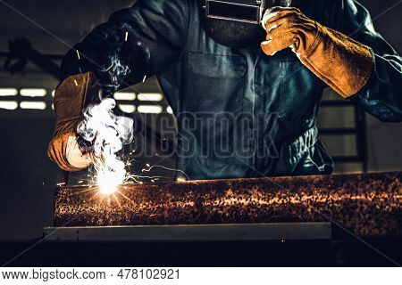 Metal Welder Working With Arc Welding Machine To Weld Steel At Factory While Wearing Safety Equipmen