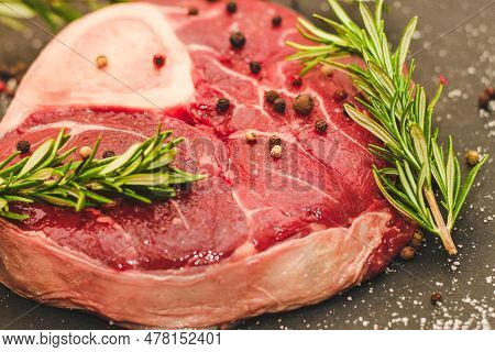 Fresh Piece Of Meat Large Beef Steak On The Bone Ossobuco With A Sprig Of Rosemary On A Black Backgr