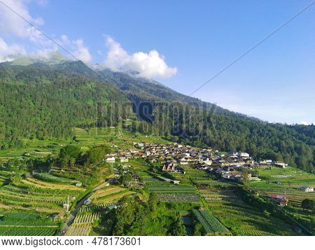 View Of Merbabu Mountain In Indonesia During Hazy Sunset With Green Village Foreground.