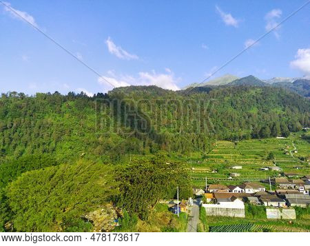 View Of Merbabu Mountain In Indonesia During Hazy Sunset With Green Village Foreground.