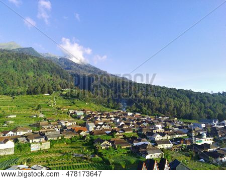 View Of Merbabu Mountain In Indonesia During Hazy Sunset With Green Village Foreground.