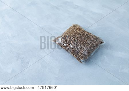 Dried Coriander Seeds In Transparent Plastic Bag On Grey Background. Natural Seasoning. Selective Fo