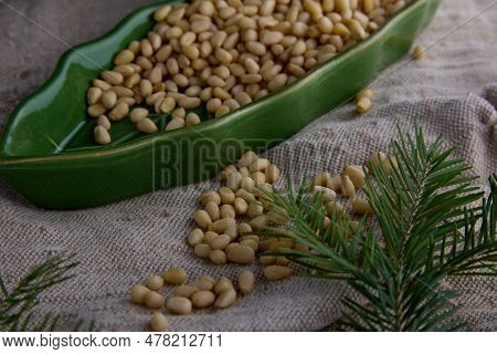 Lots Of Peeled Pine Nuts In A Green Leaf-shaped Plate On Burlap. Pine Nuts And A Coniferous Branch A