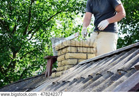 Chimney Construction, Repairs And Re-building. A Contractor Is Bricklaying A Brick Chimney On An Hou