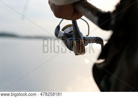 Old Man Fishing. Senior Gray Haired Fisherman Throws A Spinning From Shoreside At Sunset, Twisting A