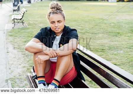 Sad Frustrated Lesbian Woman With Lgbtq Rainbow Badge On T-shirt Sitting On The Park Bench Alone. Co