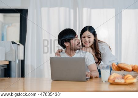 Happy Young Loving Family Couple Looking At Laptop Computer Screen, Reading Ecipes. Wife Showing Emb