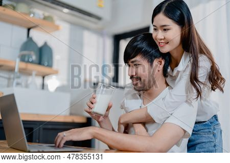 Happy Young Loving Family Couple Looking At Laptop Computer Screen, Reading Ecipes. Wife Showing Emb