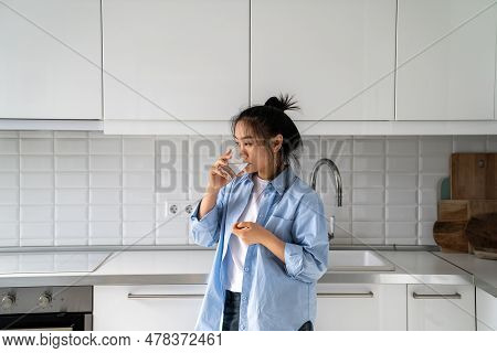 Weakened Lonely Asian Woman Drinking Glass Of Water With Probiotics Stand In Kitchen Of Home. Chines