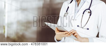Unknown Woman Doctor Iusing Tablet Computer In Her Hands, While Standing In Clinic. Medicine Concept