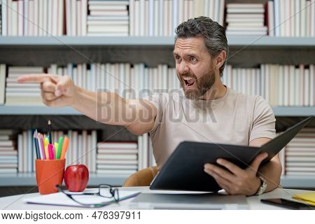 Portrait Of Sad Angry Teacher With Book In Library Classroom. Handsome Teacher In University Library