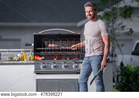 Man At A Barbecue Grill. Male Cook Preparing Barbecue Outdoors. Bbq Meat, Grill For Picnic. Roasted 