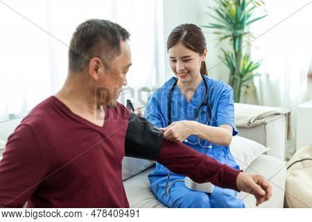 Caregiver Nurse Measuring Blood Pressure By Using Digital Sphygmomanometer Senior Patient At Home. C
