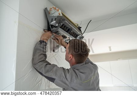Professional Man Technician In Uniform Installing Air Conditioner In Modern Apartment On Wall Near W