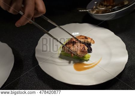 Chief Cook Putting Grilled Meat Piece Using Tweezers On Green Vegetables Puree White Plate With Sauc