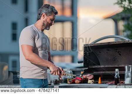 Man At A Barbecue Grill. Male Cook Preparing Barbecue Outdoors. Bbq Meat, Grill For Picnic. Roasted 