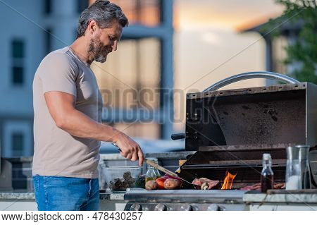 Man Cooking Meat On Barbecue In The Backyard Of The House. Handsome Man Preparing Barbecue. Barbecue