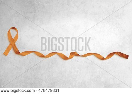 Photo Of Orange Ribbon With Curled End Atop A Light Concrete Background. Plenty Of Copy Space.