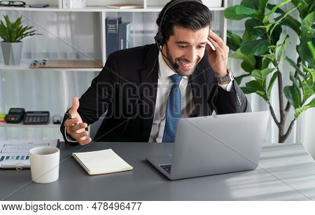 Male Call Center Operator Or Telesales Representative Siting At His Office Desk Wearing Headset And 