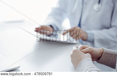 Doctor And Patient Sitting At The Table In Clinic While Using Tablet Computer. The Focus Is On Femal