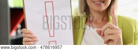 Portrait Of Smiling Woman Holding Clipboard With Red Exclamation Point. Interjection And Exclamatory