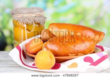 Empanadillas al horno frescos con mermelada de frutas, en la mesa de madera, sobre fondo brillante