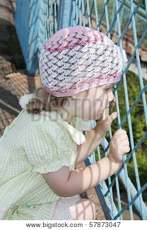 Little Pretty Girl Looks Through Blue Grid At Summer Sunny Day
