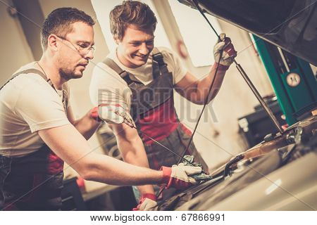 Two mechanics checking oil level in a car workshop