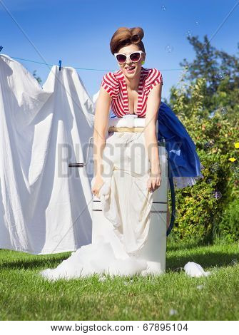 Pin up style photo of woman doing laundry using vintage wringer washing machine
