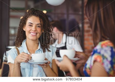 Portrait of smiling pretty customer holding cup of coffee in front of barista at coffee shop