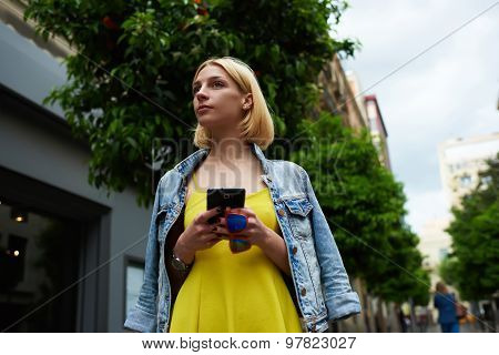 Young student girl browsing internet on mobile phone while standing on tree background in the city
