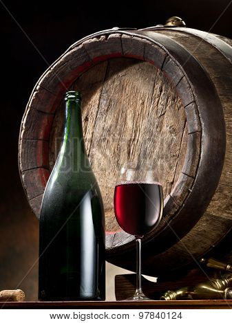Still-life with glass of wine, bottle and barrel on the table in the cellar.