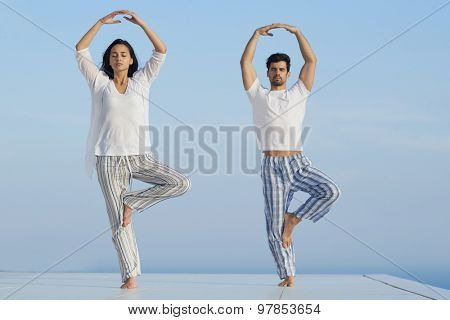 young couple practicing yoga at sunset in modern home terace with ocean and sunset in background