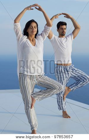 young couple practicing yoga at sunset in modern home terace with ocean and sunset in background