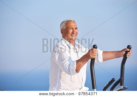 healthy senior man working out on gym treadmill machine at modern home terace with ocean view
