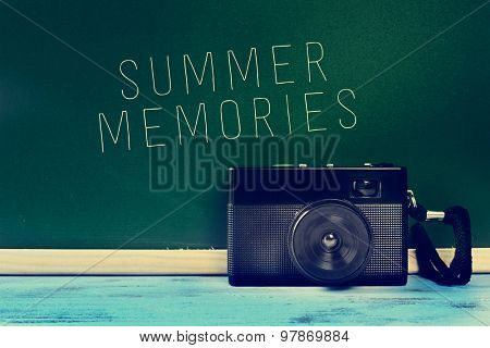 a retro camera on a rustic blue wooden surface and the text summer memories written on a green chalkboard, with a filter effect