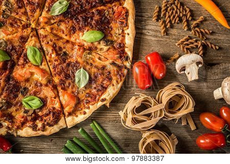 Italian food background with pizza, raw pasta and vegetables on wooden table
