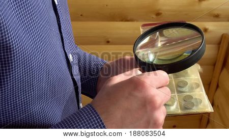 numismatist considers old coins through magnifying glass.
