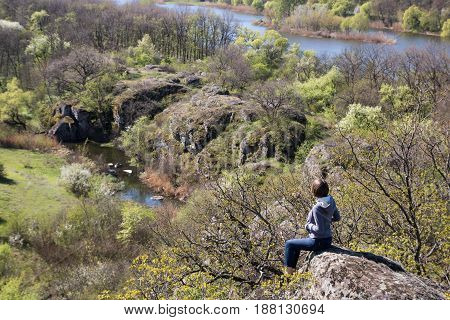 Caucasian Female Sitting On A Big Stone Above The River And Forest, Spring Time