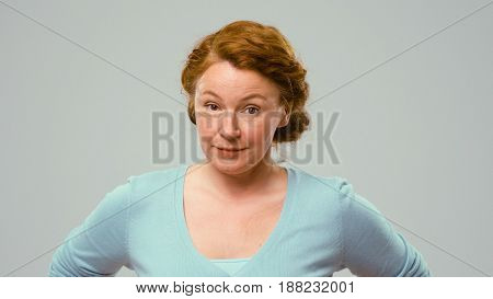 Mid aged actress showing emotions of claim. Actress in studio shows the emotion of claim. Close-up portrait of an actrees in light blue jumper. Actress with curly red hair shows the emotion of doubt.