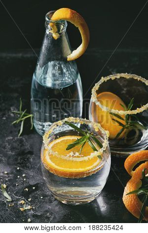 Tonic water cocktail with rosemary and orange. Two glasses and bottle with zest sugar and bubbles over black texture background. Refreshing beverage alco non alcohol