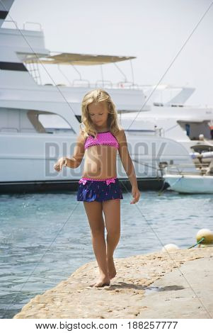 Beautiful girl strolls along the shore of the stone on the background of yachts.